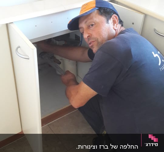 אדם מתקן צנרת מתחת לכיור במטבח